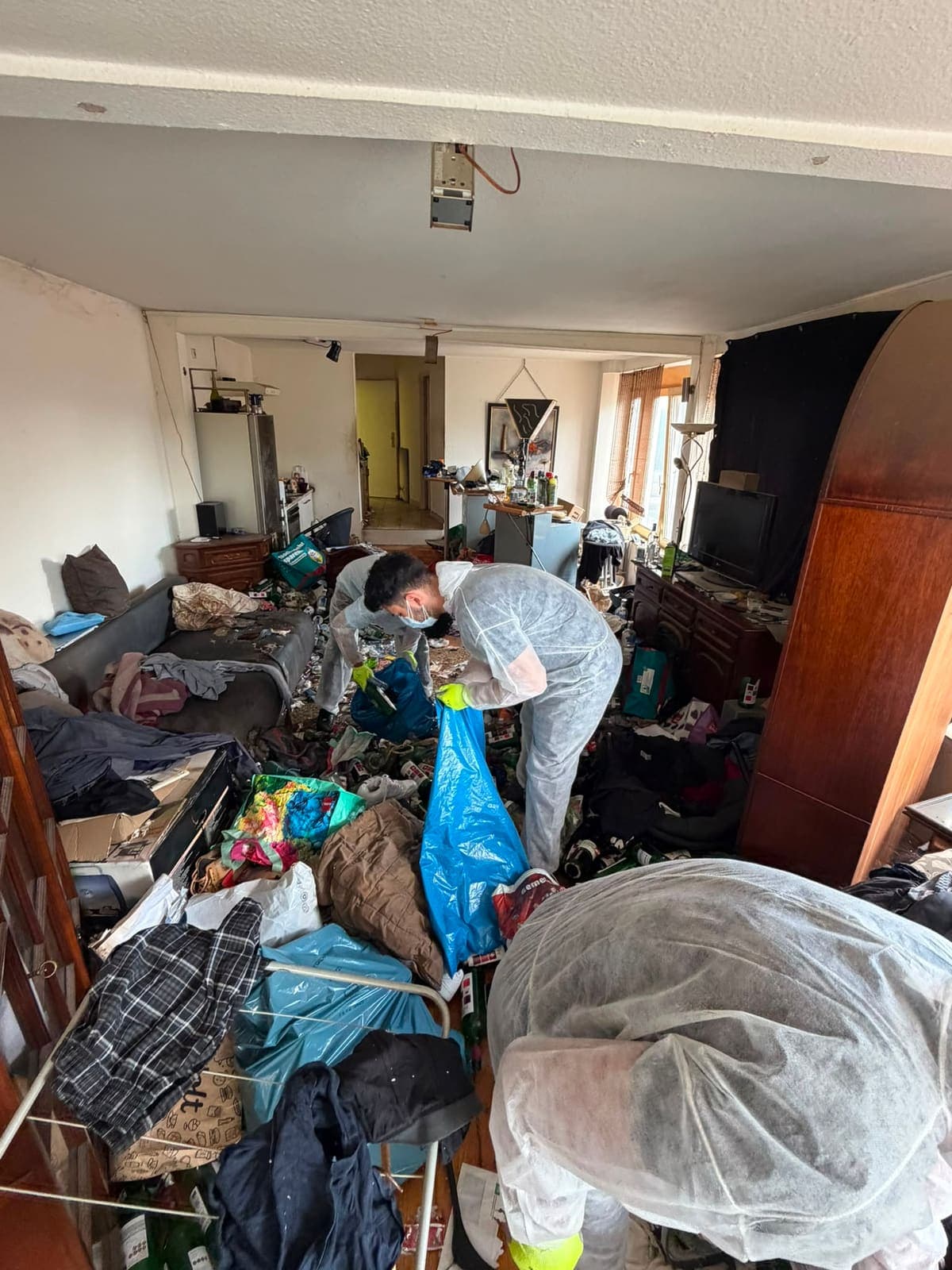 Mitarbeiter in Schutzanzug und Handschuhen räumt eine stark vermüllte Wohnung